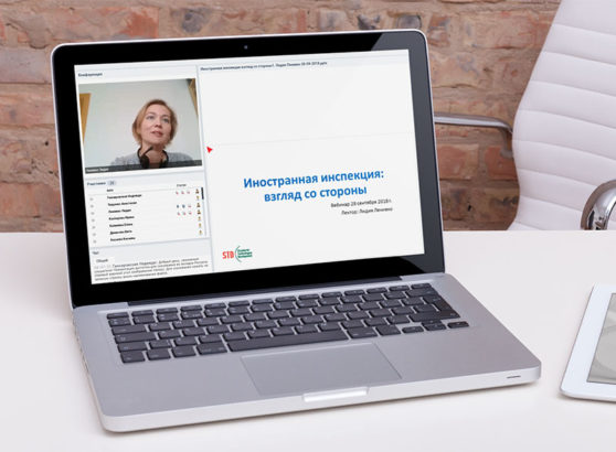 A silver laptop open on a white office desk displaying an online regulatory webinar interface with a live video feed of Lidia Lianiuka Lenivko and a slide titled 'Foreign Inspection: An Outside Perspective' in Russian.