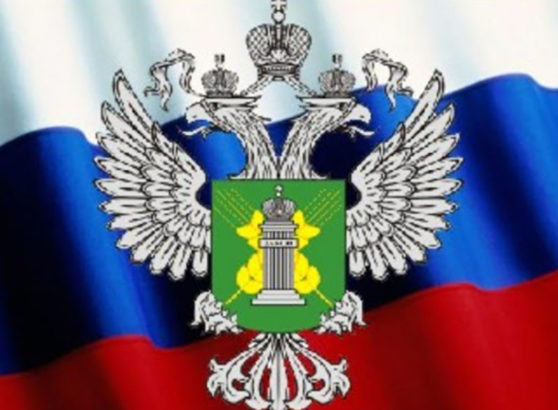 El escudo de armas oficial del Servicio Federal de Vigilancia Veterinaria y Fitosanitaria de Rusia (Rosselkhoznadzor), que muestra un águila bicéfala plateada con un escudo verde central y una columna dorada, sobre el fondo de una bandera tricolor rusa ondeando.