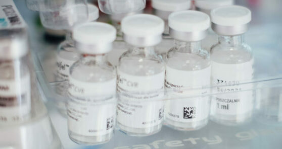 Primer plano de varios viales de vidrio transparente de 1 ml para uso veterinario, con tapones y cápsulas flip-off de color blanco, organizados en una bandeja plástica transparente dentro de una planta o laboratorio, mostrando las etiquetas impresas con un código Data Matrix bidimensional para trazabilidad.